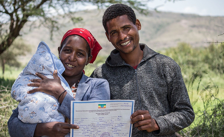 A father and mother hold up a printed paper, a newborn is in the mother's left hand.