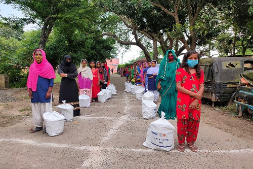Women and girls wearing facemasks queue along a grid drawn in chalk on the ground to ensure physical distancing during the dignity kit distribution.