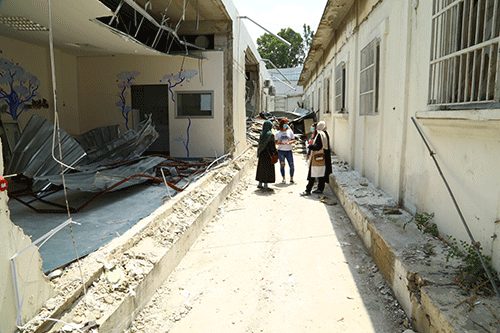 An assessment team stands in a destroyed part of a hospital in Karantina. Around them are rubble and exposed rebar.