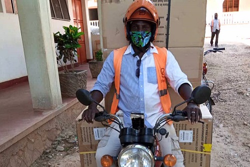 A SafeBoda driver prepares to drive away on a motorcycle carrying four large boxes of reproductive health cargo.