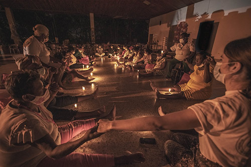 Pregnant women sit in a circle in a dimmed, candle-lit room, holding hands.