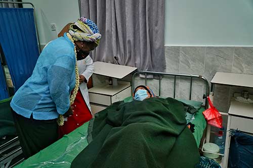 Dr. Kanem speaks to a woman lying on a bed at a maternity ward. Both are wearing face masks.