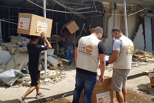 UNFPA staff members carry boxes of PPE over rubble. 