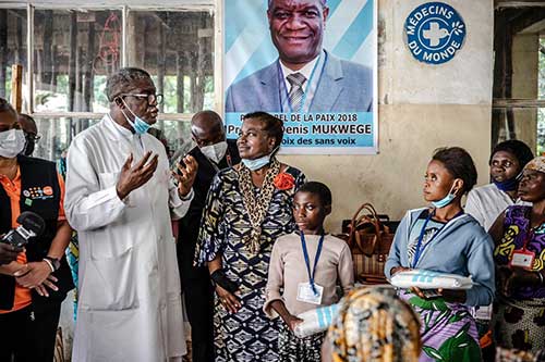 A tall doctor in a white coat speaks with UN personnel and other people. 