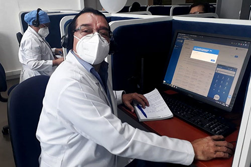 A doctor wearing a face mask sits at a computer.