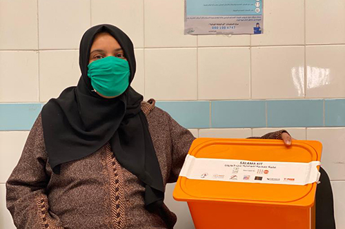 A pregnant woman wearing a face mask sits in a health centre with her SALAMA kit, which contains supplies and information to help prevent COVID-19 transmission.