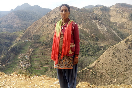 Hira stands against a cliff side, with tall mountains and terraced fields behind her.