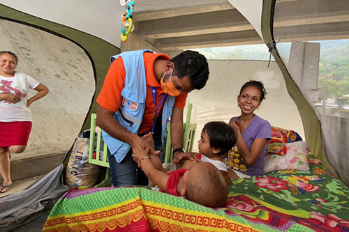 A doctor wearing a UNFPA vest checks up on an infant, who is lying on an air mattress inside a tent.