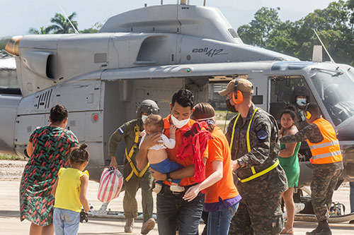 Families are assisted by humanitarian workers using a helicopter.