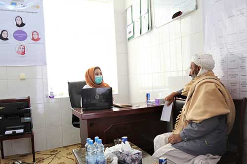 Dr. Freshta Fahim, wearing an orange head scarf and face mask, speaks to Aref, wearing a brown shawl. 