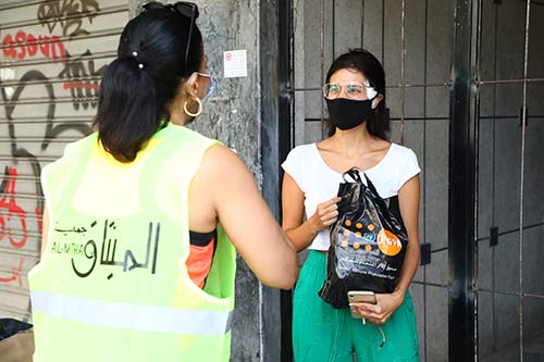 Rima passes a dignity kit to a young woman with a bandage on her face.