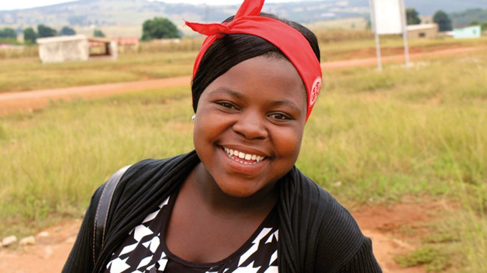 Takhona stands in a field in Eswatini. She is smiling broadly.