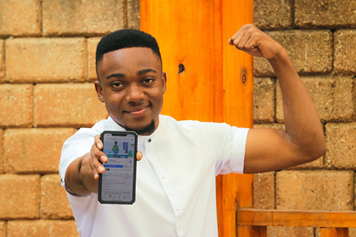 A young man shows off an app on his mobile phone with one hand, and flexes the bicep of his other arm.