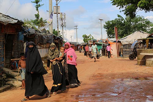 Women walk down a path of a Rohingya refugee camp.