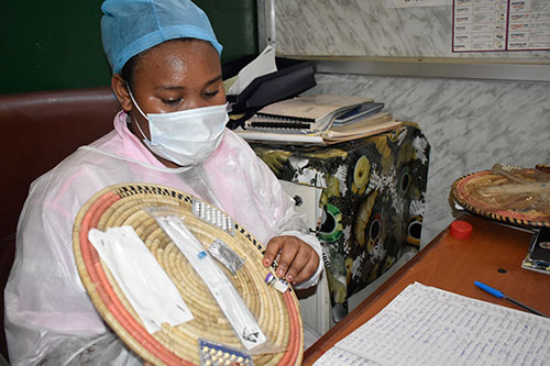 A midwife wearing a mask and hair covering shows clients family planning options available at the clinic, including oral contraceptive pills, injectables and implants.