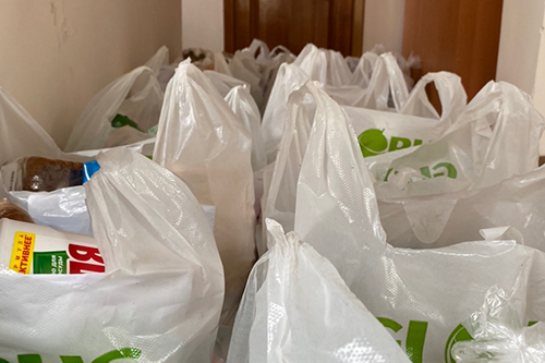 Plastic bags full of food items are accumulated near a door for delivery.