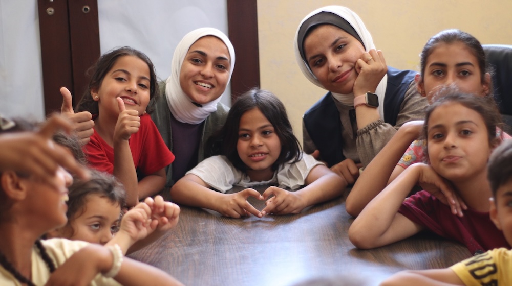 Two adult women sit with a group of young children around a table