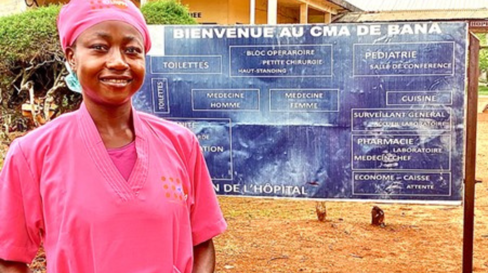  A midwife dressed in a pink uniform stands beside a sign.