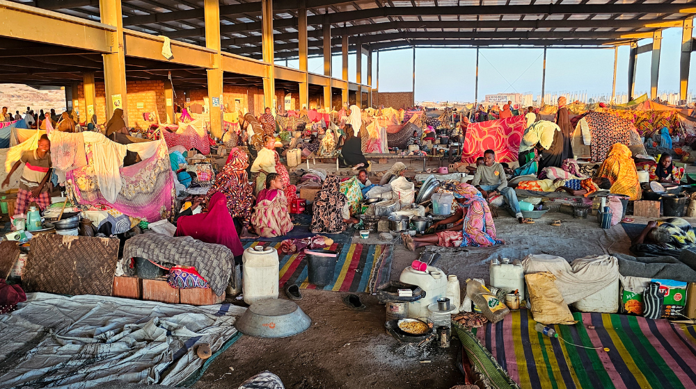 A large semi-covered space is full of people, blankets, tents and belongings