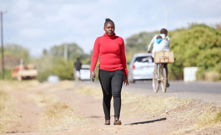 A woman walks along a road as cars and bikes pass by.