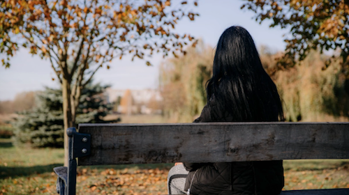 A woman sits on a park bench with her back to the camera.