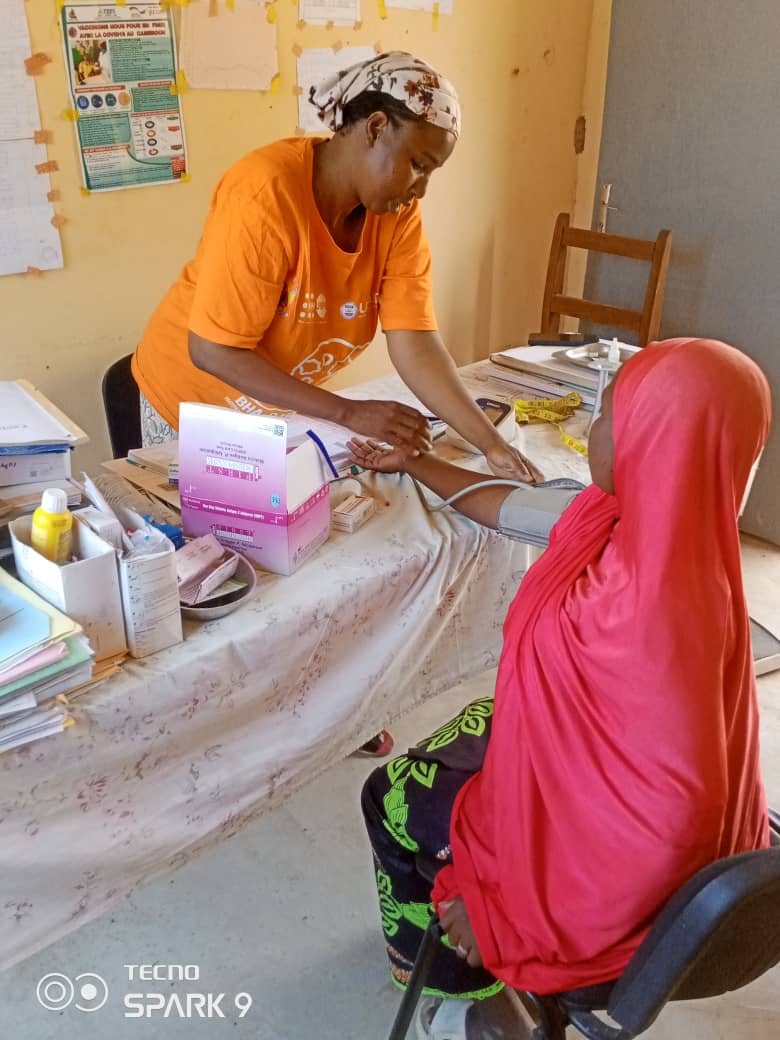 A woman stands and takes the blood pressure of a seated woman