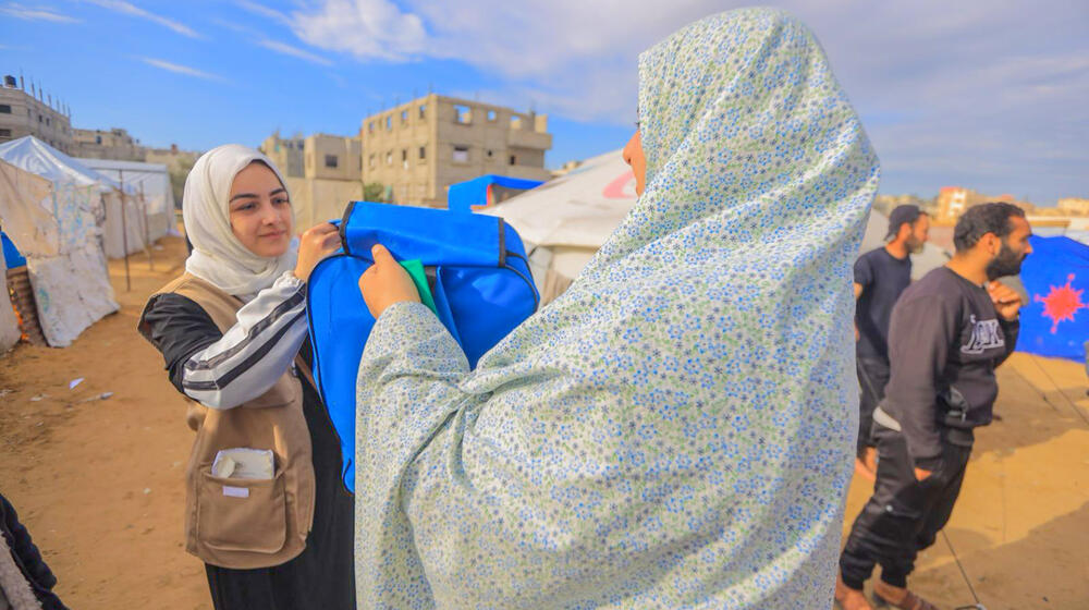 Two women in a displacement camp examine a blue bag