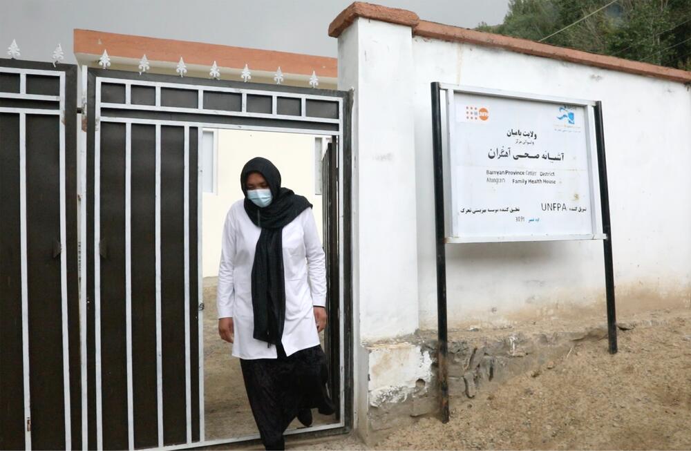 A woman wearing a mask walks through the door of a gate to a building