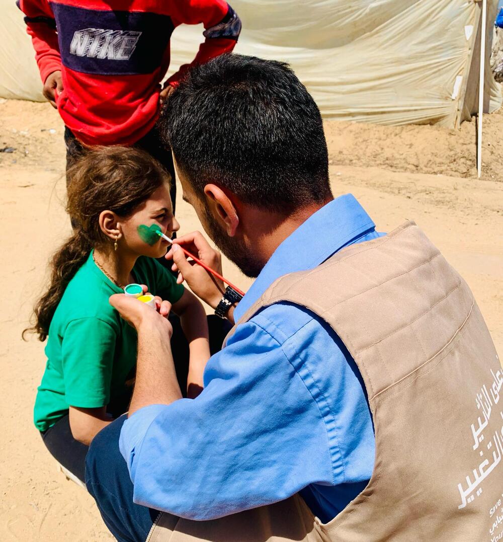 A man paints a green heart onto a young girl’s cheek