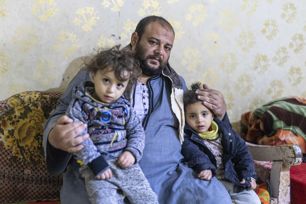 A man sits on a couch with two young girls on his lap, embracing them