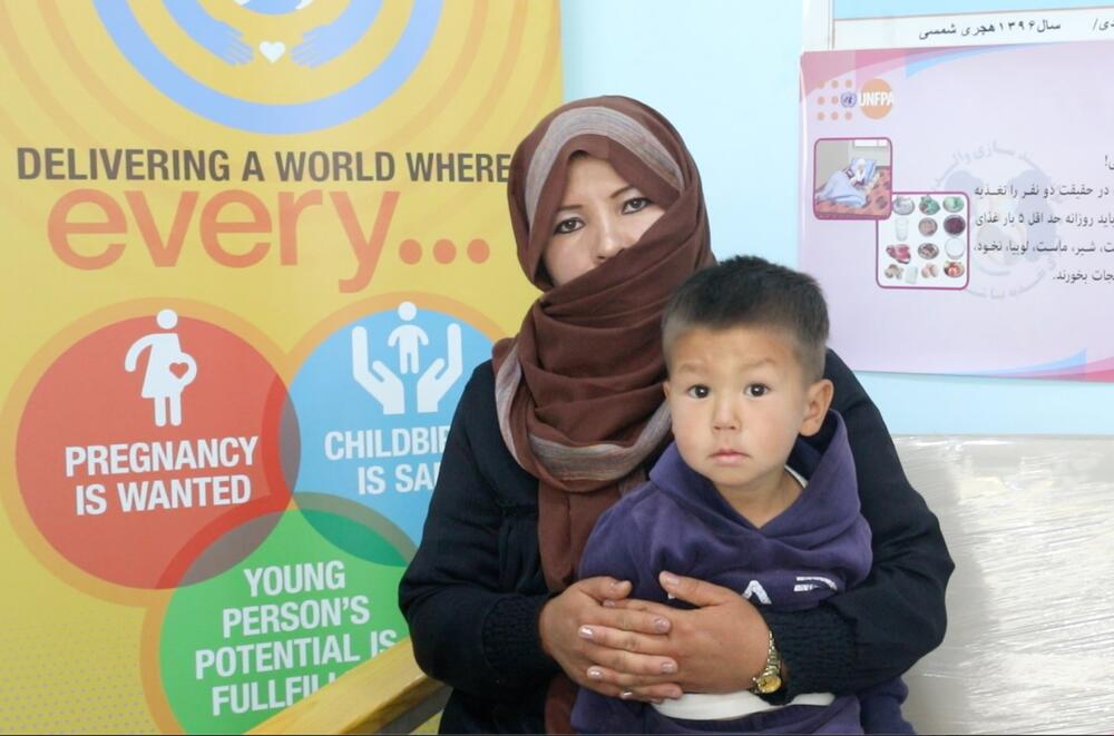 A woman holds a young boy in front of a UNFPA poster