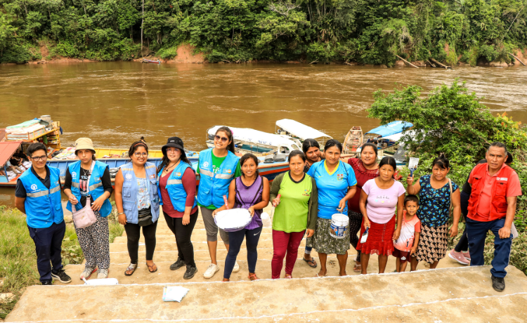 Catorce personas miran a la cámara. Algunas tienen chalecos azules del UNFPA; otras tienen cubos con pintura blanca. Todas están de pie en las escaleras del puerto rodeadas por la selva.