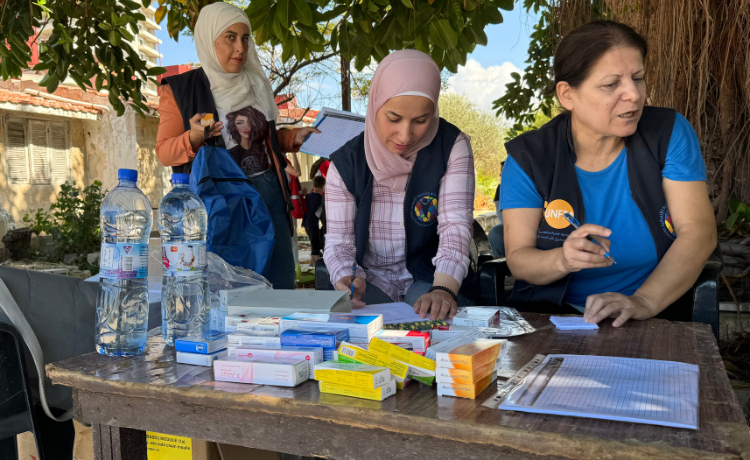 Des femmes disposent des médicaments et des fournitures sur une table, sous un arbre. Elles sont vêtues de gilets noirs portant les logos de l’UNFPA et de Mosaic.