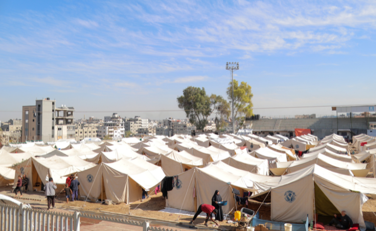 A view of multiple white tents with some displaced people in the foreground