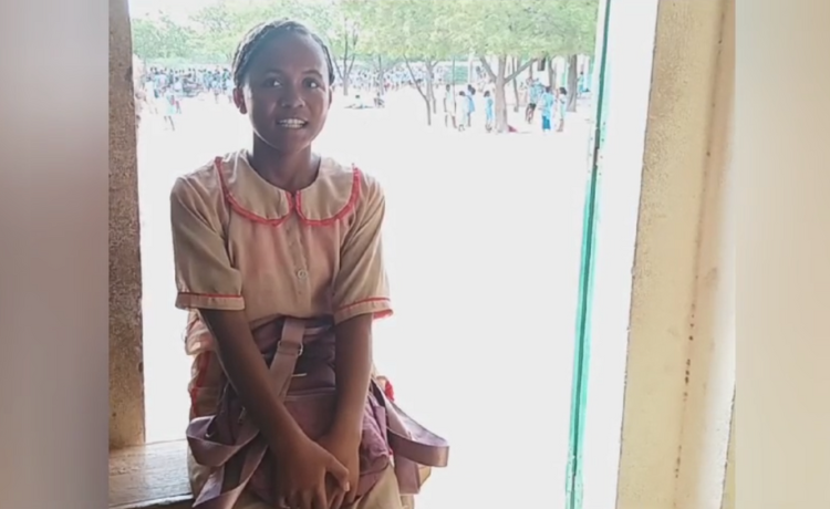 A teenage girl in school uniforms smiles in front of a courtyard