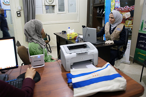 A Syrian woman speaks with an aid worker sitting at a computer. 