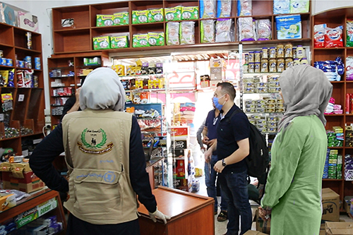 Syrians and aid workers speak in a store stocked with food and hygiene supplies.