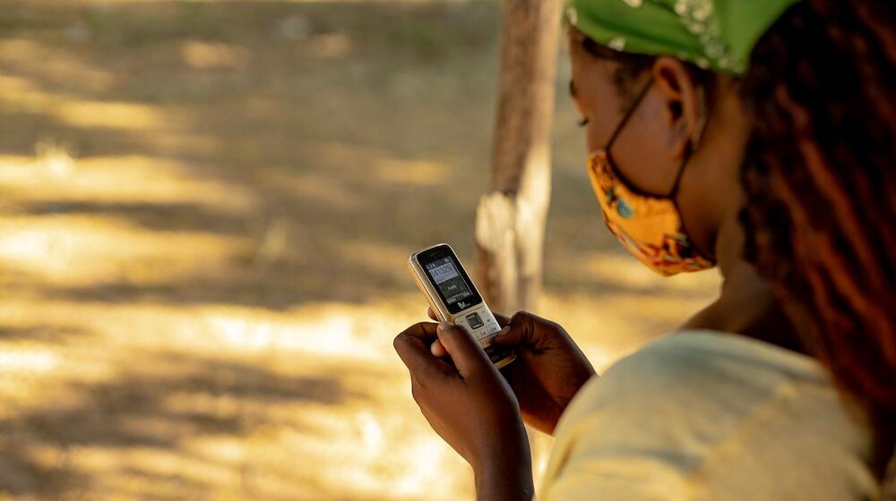 A young girl looks towards the mobile phone she is holding. 