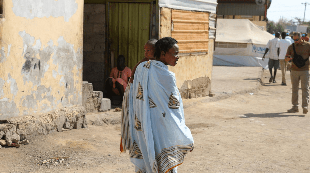 Woman holding a child walks through town.