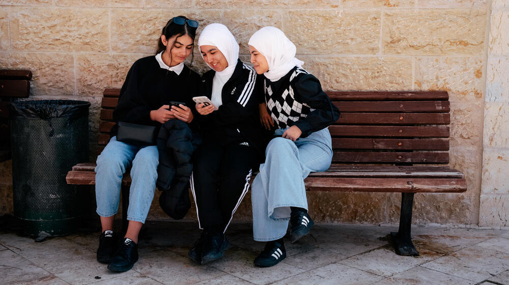 Three teenage girls look towards the mobile phones in their hands. 