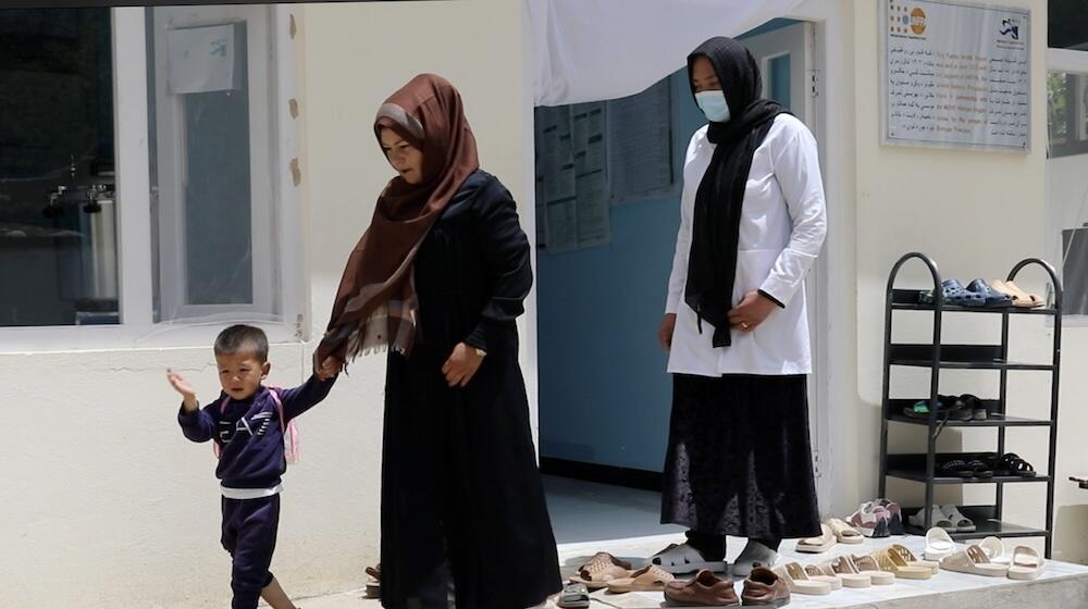 A woman holds a young boy’s hand as another woman stands behind them