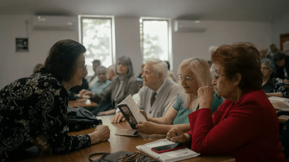 Personas de edad sentadas detrás de unas mesas en un taller de literatura