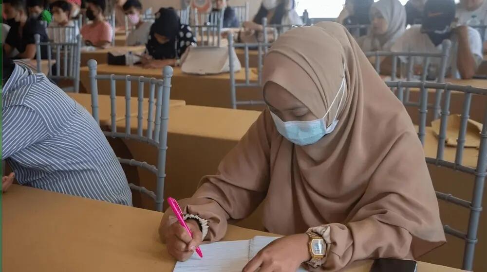 A young woman sits and writes at a table.