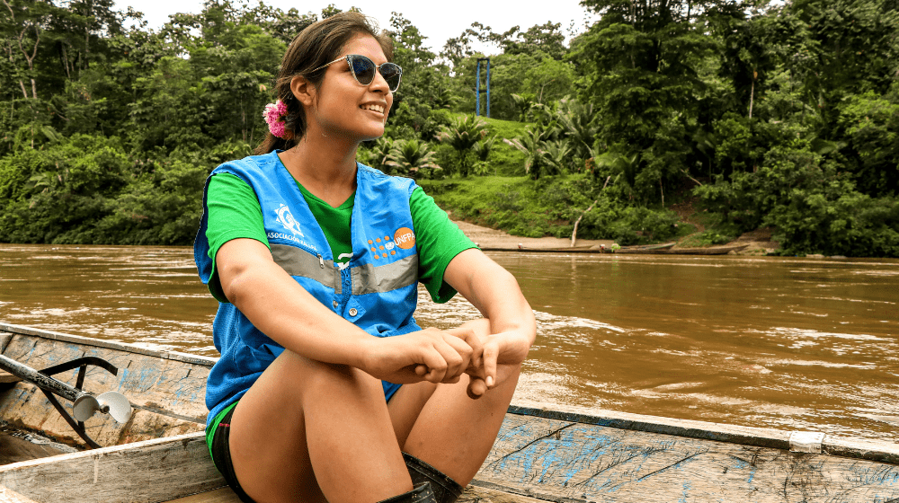  Une jeune femme est assise dans une barque en bois sur un fleuve entouré par la jungle.