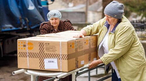 Two women handle a cart with large boxes
