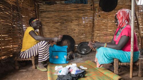 Deux filles sourient, assises dans une hutte, et examinent le contenu d’un kit dignité étalé au sol