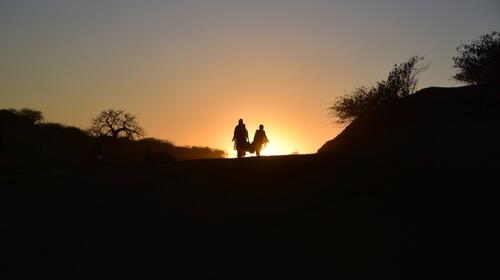 Two women carry a basket and walk into the hills at dusk.