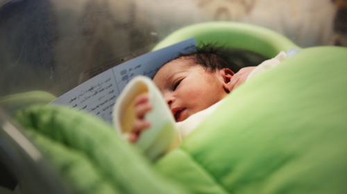 Una bebé envuelta en una manta verde en una cuna de hospital.