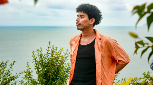  A young man in an orange shirt stands overlooking the sea