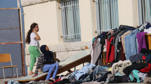  Des jeunes filles sont assises devant une école publique qui sert de refuge. Près d’elles, des meubles sont recouverts de piles de vêtements colorés.